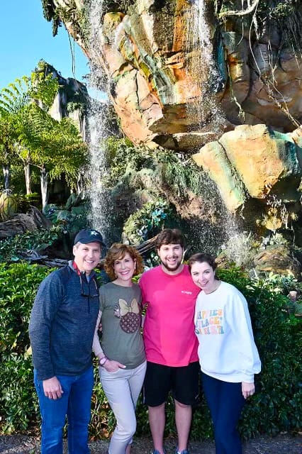 family of 4 adults standing in front of lush landscaping on a multi-generational disney world trip