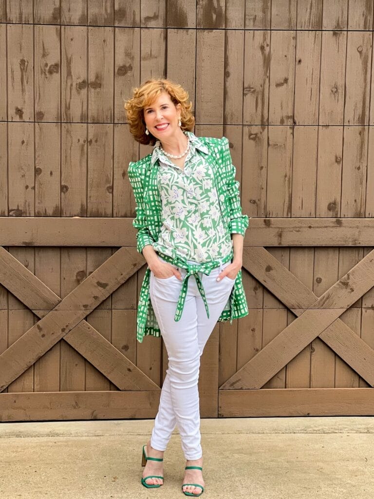 woman over 50 wearing circuit jacket, white the skinny jeans, and bloom top from cabi 2022 spring collection unbuttoned with top showing and belt around waist of jeans