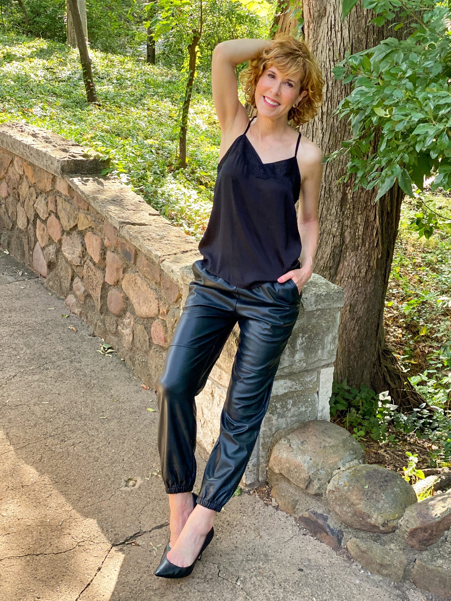 woman over 50 posing outside by a tree wearing nordstrom made brands spring top styles like this Eyelash Lace Trim Satin Crop Camisole and black pleather joggers