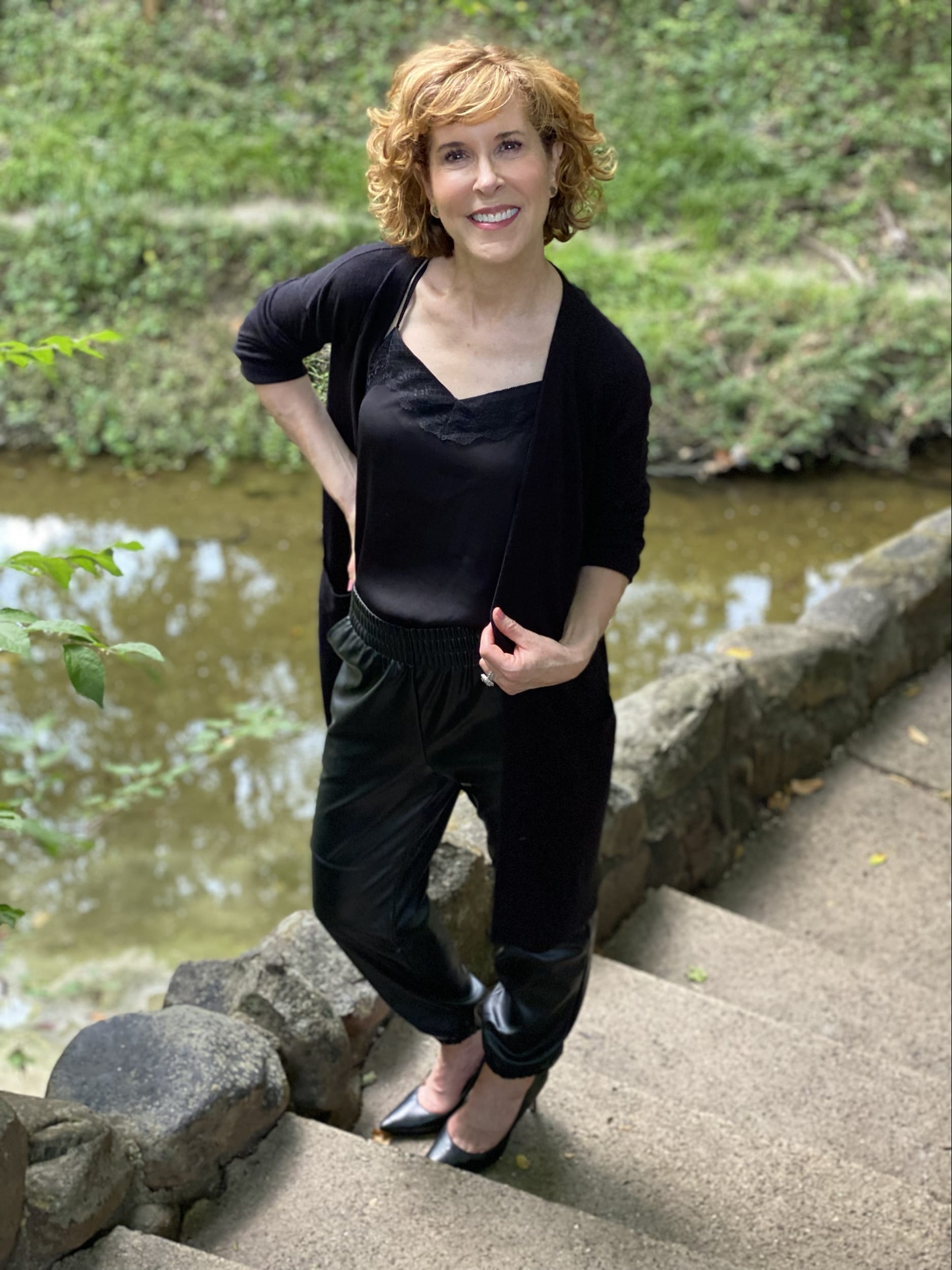 woman over 50 posing by a stream wearing nordstrom made brands spring top styles like this Eyelash Lace Trim Satin Crop Camisole black cardigan and black joggers