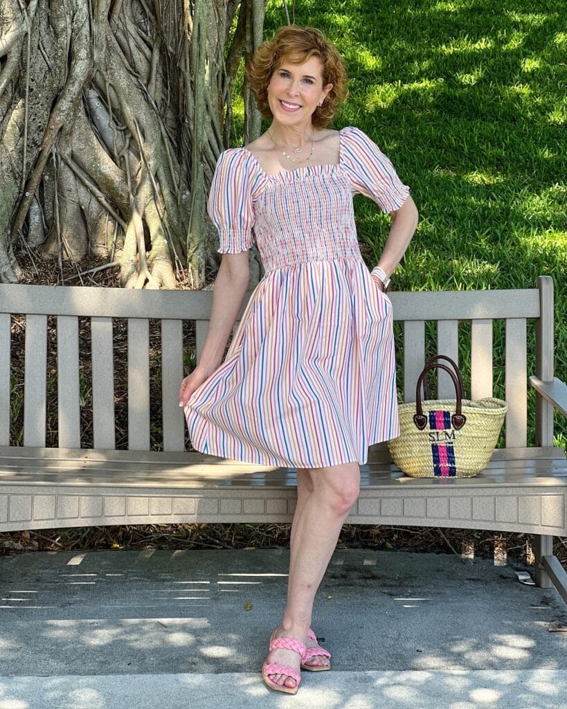 woman over 50 posing in front of a bench wearing a colorful striped dress