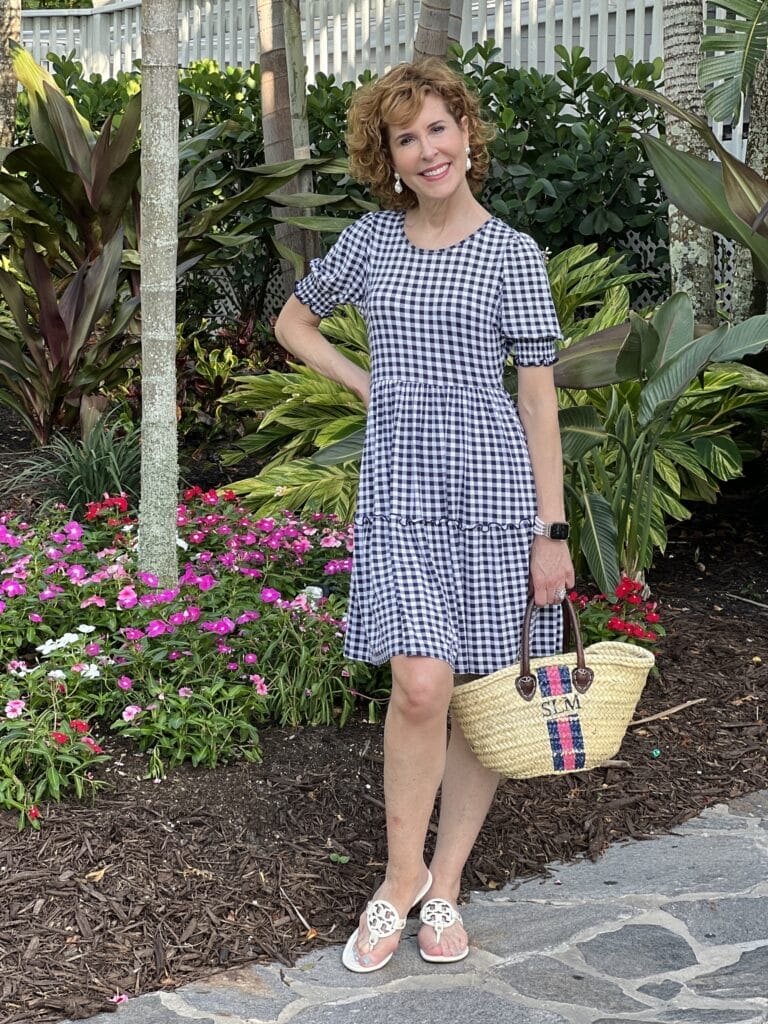 woman over 50 posing in a garden wearing a blue and white gingham draper james tiered dress