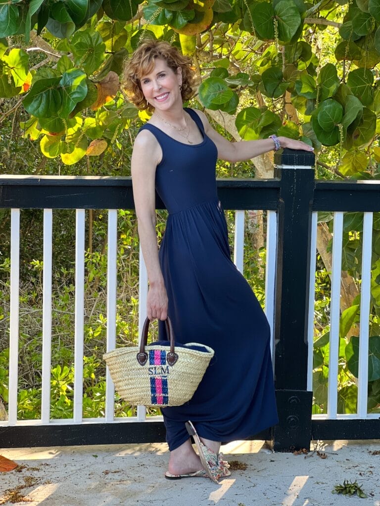 over 50 woman wearing a navy maxi dress and holding a personalized straw handbag