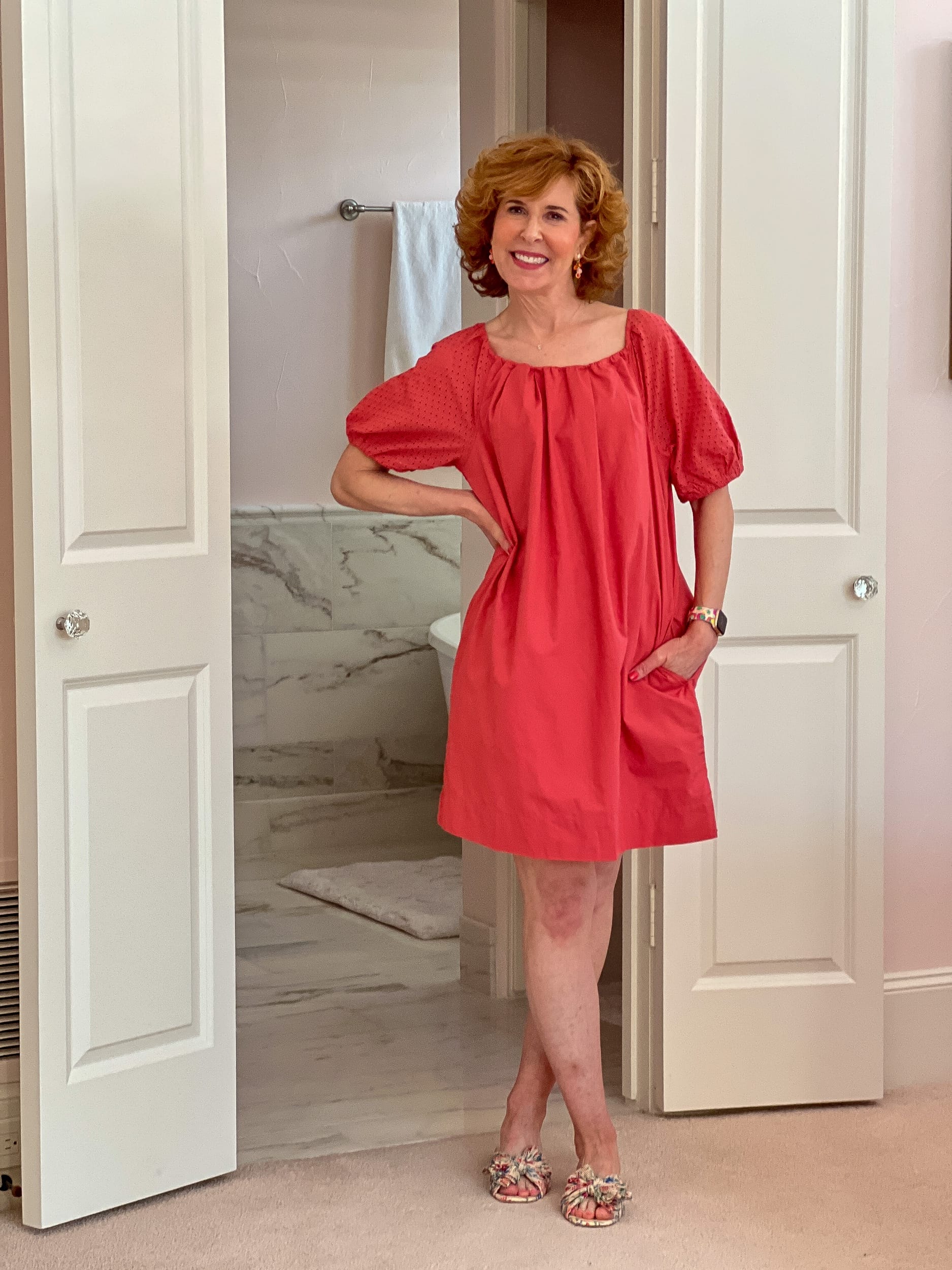 woman over 50 standing in bathroom doorway wearing a coral Walmart shift dress 