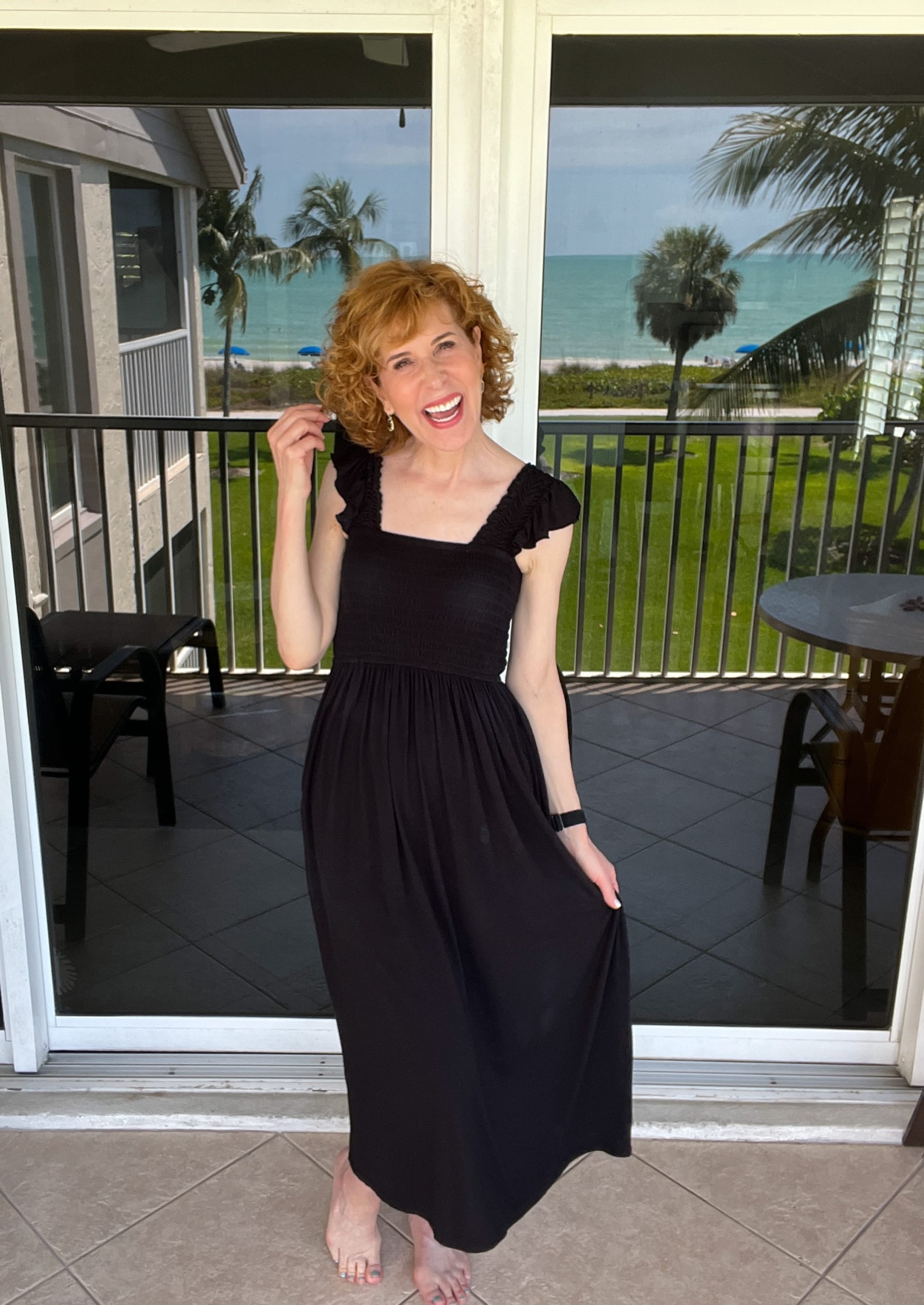 woman standing on a balcony with the reflection of a beach in the background wearing nordstrom's moonlight dress in black