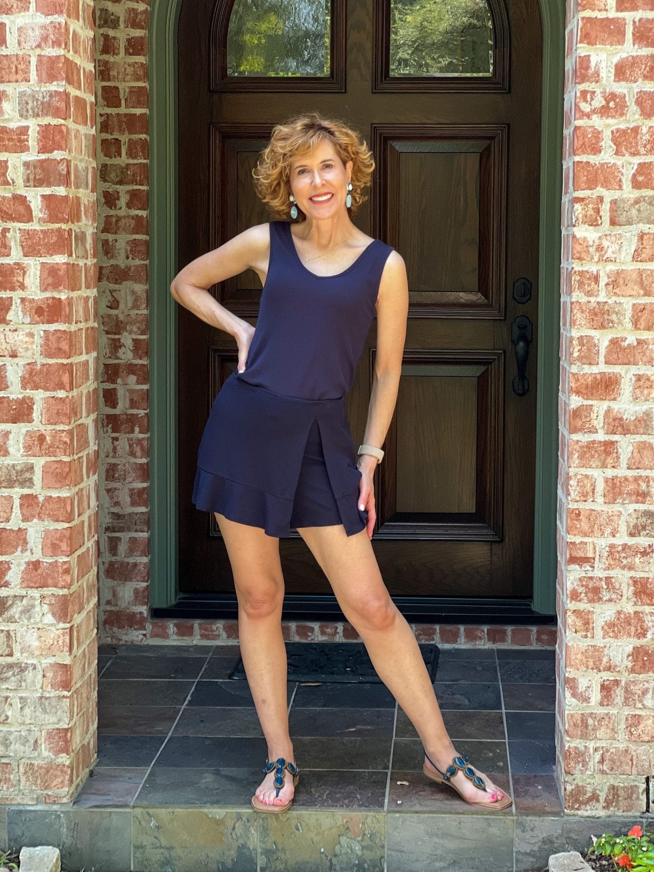 woman wearing cabi busy tank and golf cart skort in navy standing on porch