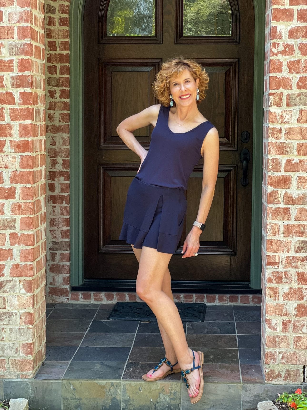 woman wearing cabi busy tank and golf cart skort in navy standing on porch