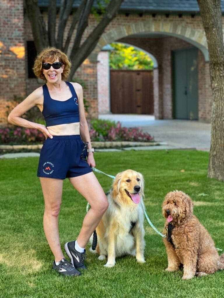 woman standing in front yard with with 2 dogs on leash wearing mighty health sports bra & shorts