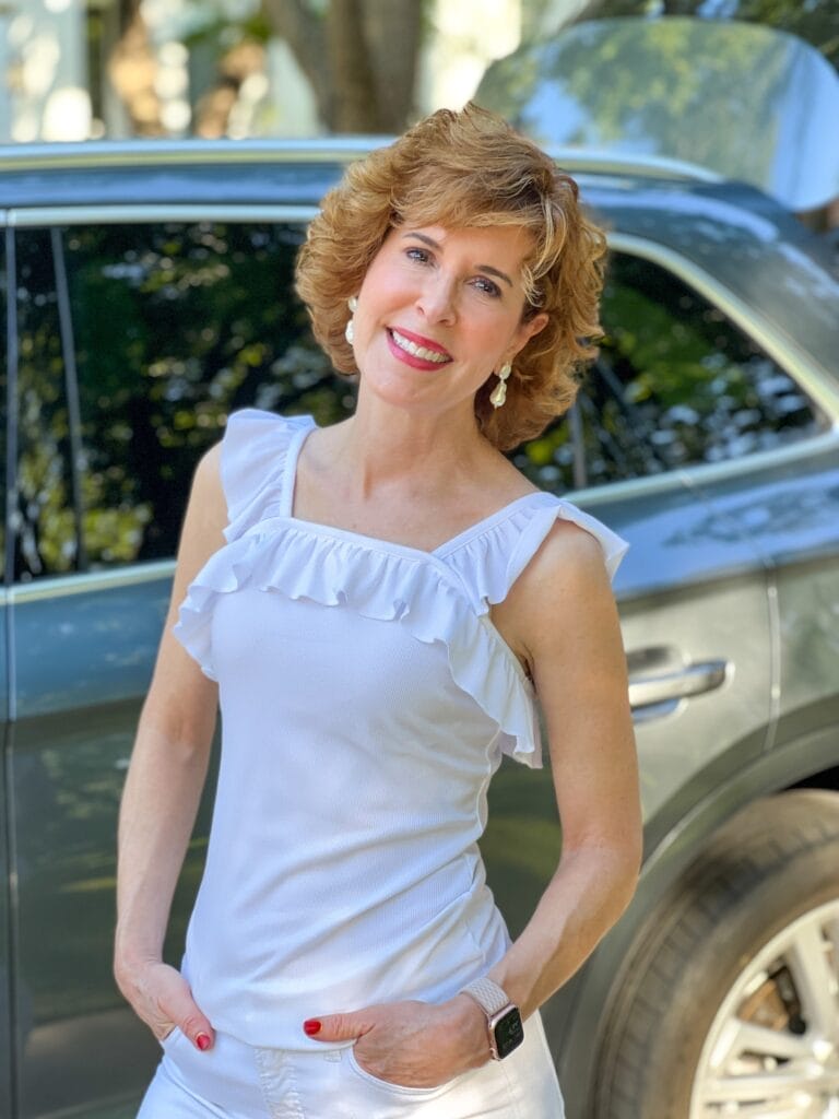 woman wearing ruffle sleeveless top in white standing near a car