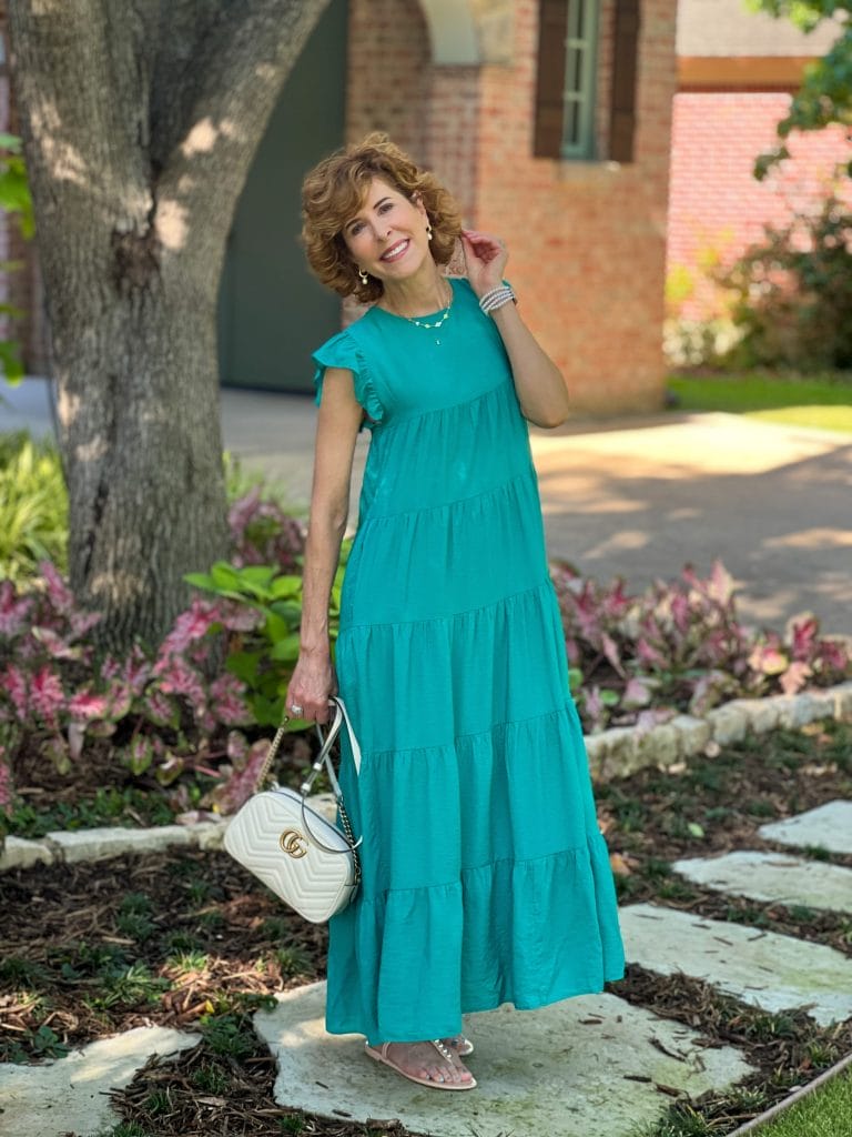 woman wearing teal lara dress from avara and white purse standing in front yard