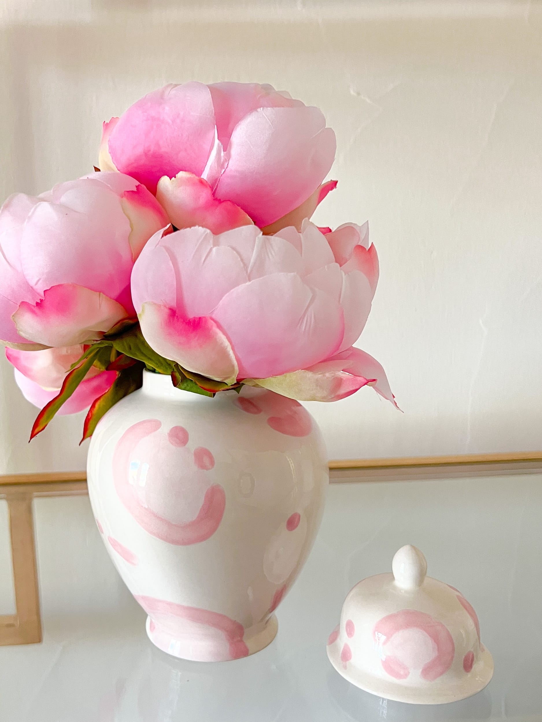 small pink leopard ginger jar filled with silk pink peonies sitting on glass shelf