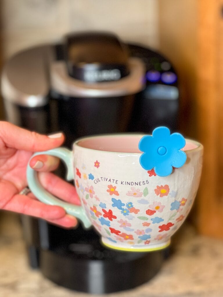 woman's hand holding a cultivate kindness latte mug with blue tea infuser in front of a keurig