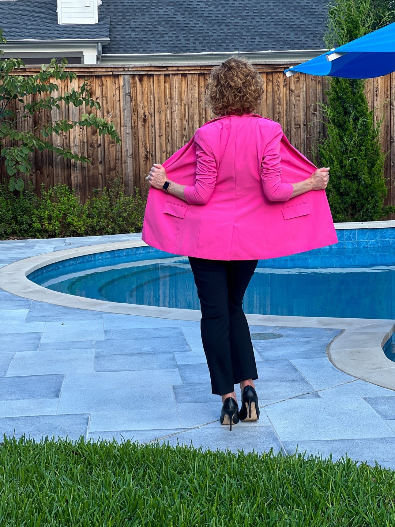woman with her back to the camera wearing hot pink amazon blazer and black pants standing by a pool