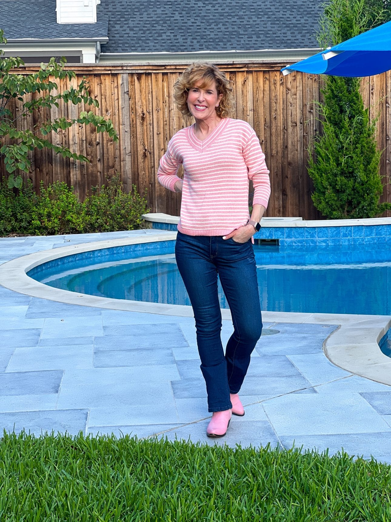 woman posing by a pool wearing talbots oink striped Linen V-Neck Sweater, wit & wisdom boot cut jeans and pink cowboy boots