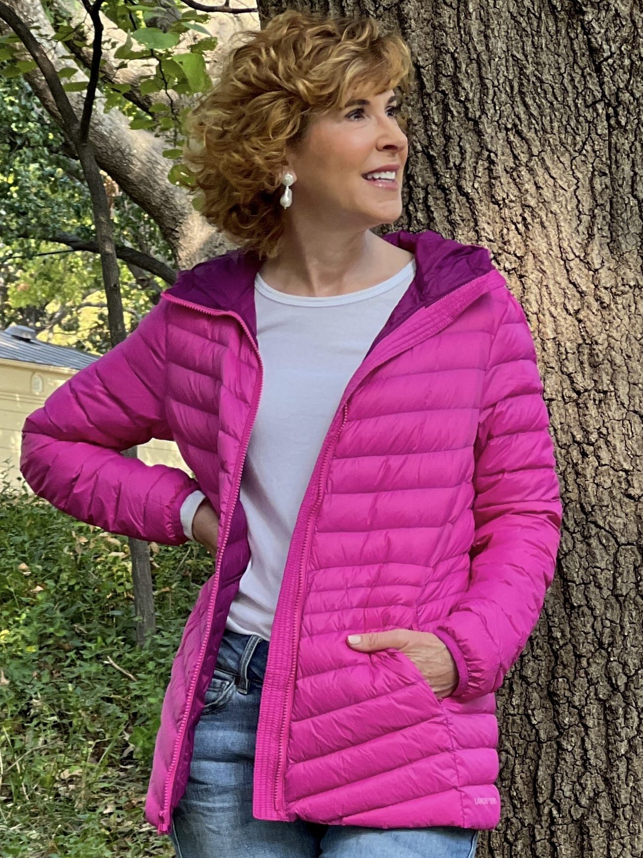 woman wearing land's end Ultralight Packable Down Jacket in hot pink and cropped jeans with hot pink sneakers standing by a tree in the park