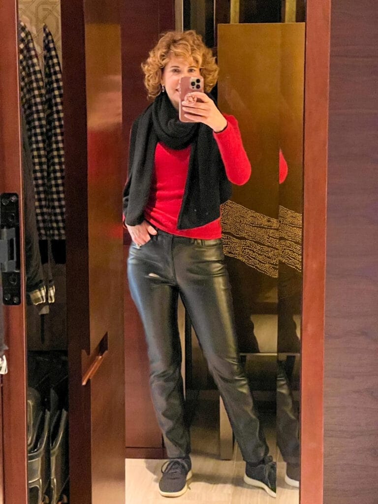 woman taking mirror selfie wearing red sweater, black cashmere scarf, good american faux leather black jeans and black sneakers