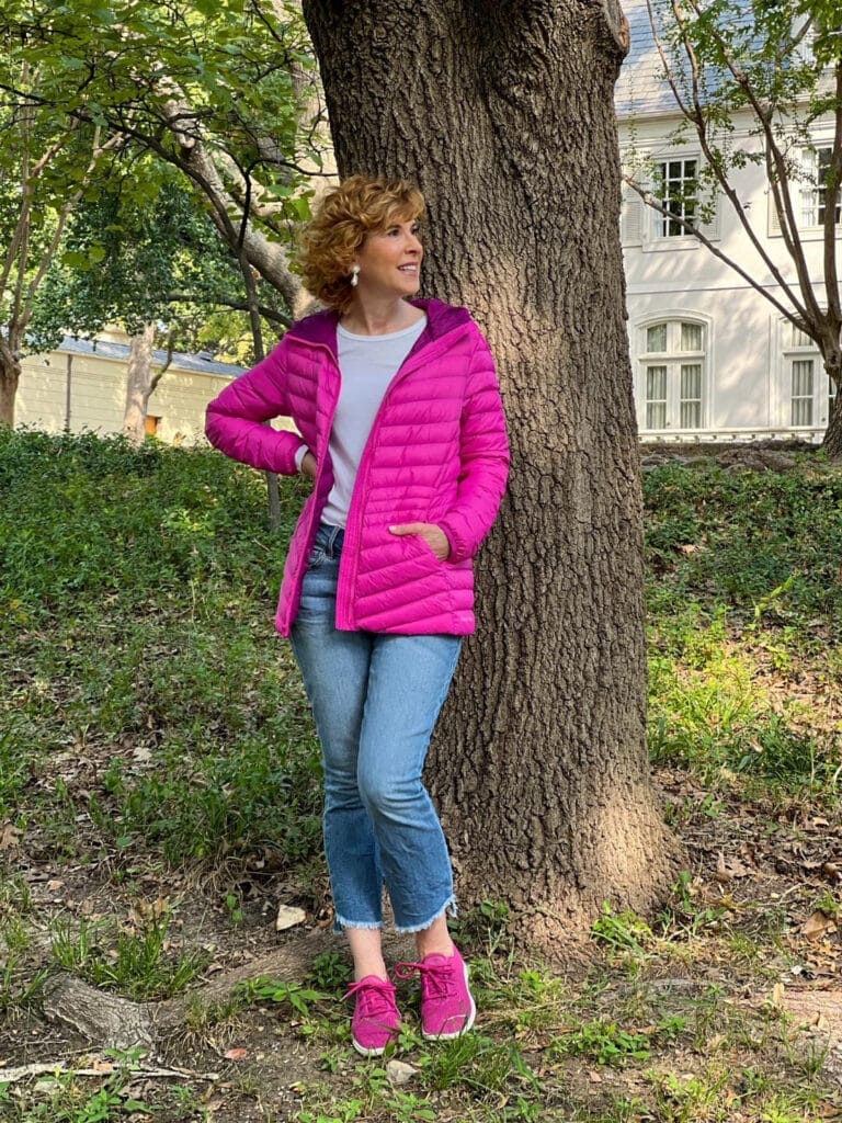 woman wearing land's end Ultralight Packable Down Jacket in hot pink and cropped jeans with hot pink sneakers standing by a tree in the park