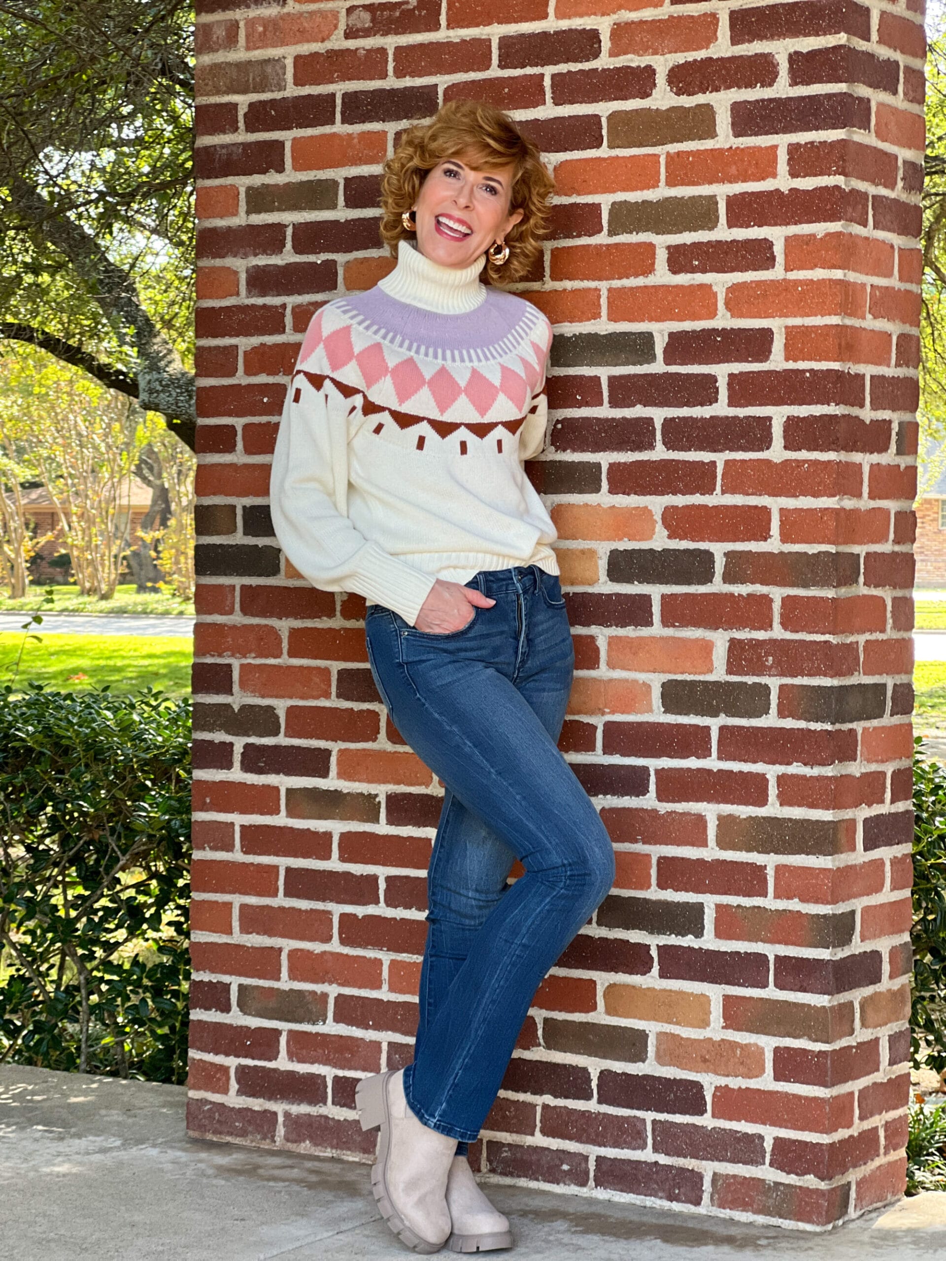 Woman over 50 standing by a brick wall wearing Free Assembly Women's Fair Isle Sweater, Sofia Jeans by Sofia Vergara Women's High Rise Skinny Kick Bootcut Jeans, and Madden NYC Women's Lug Sole Chelsea Booties all from Walmart