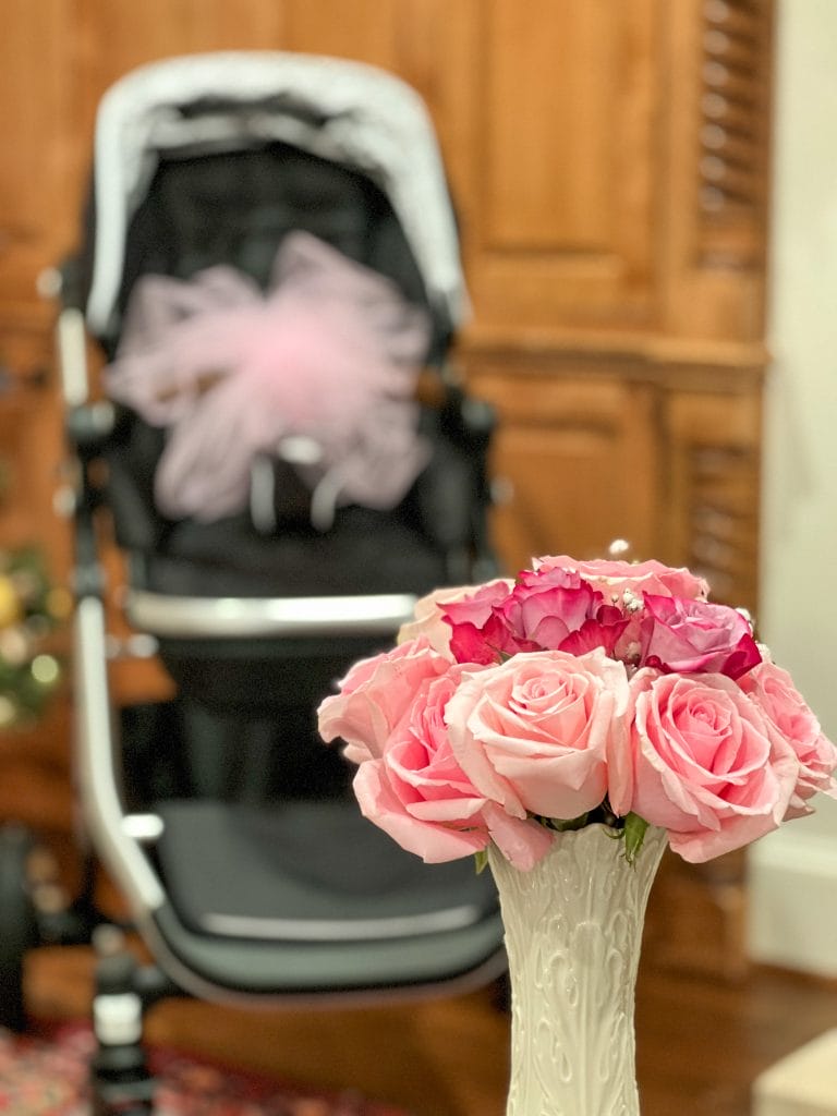pink roses in cream vase in foreground stroller gift in background