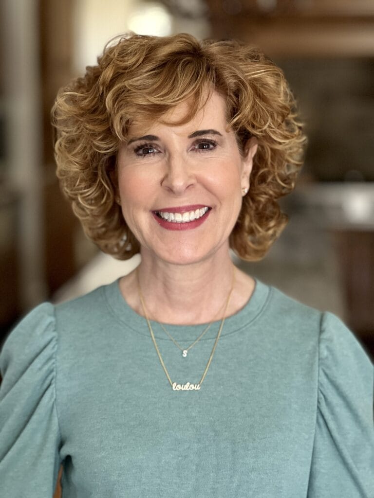 woman over 50 wearing blue/green puff sleeve Amazon tee and "S" initial pendant necklace and script necklace that says "loulou"