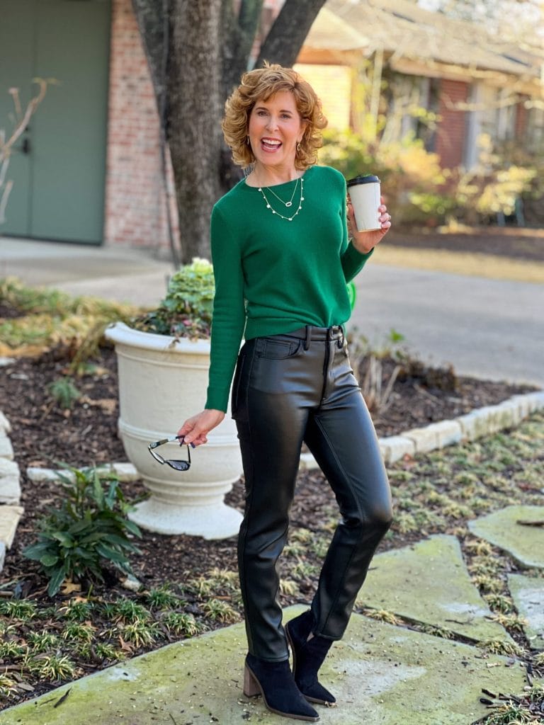woman standing in yard wearing green cashmere sweater and faux leather jeans