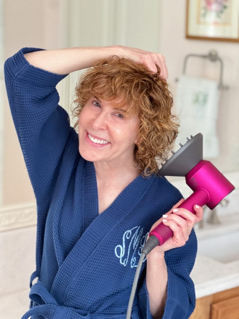 woman over 50 in a bathroom styling her curly hair with a diffuser