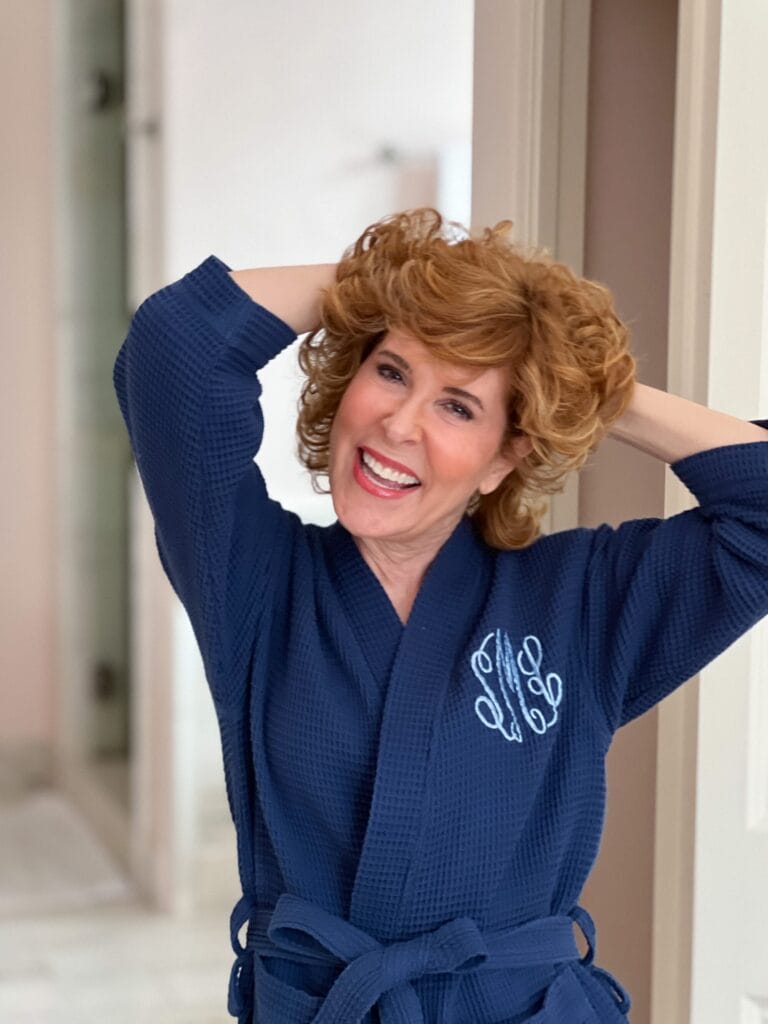 woman in blue monogrammed robe tousling her curly hair