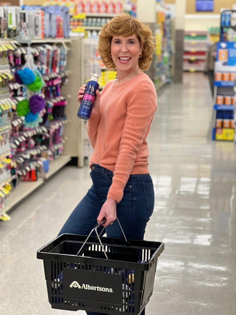 Woman over 50 shopping at albertsons holding hair biology product in a store aisle