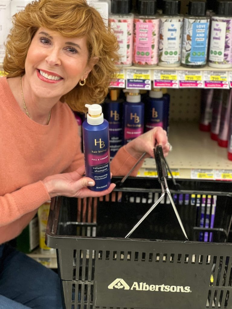 woman holding albertson's shopping basket and hair biology product kneeling by store shelves