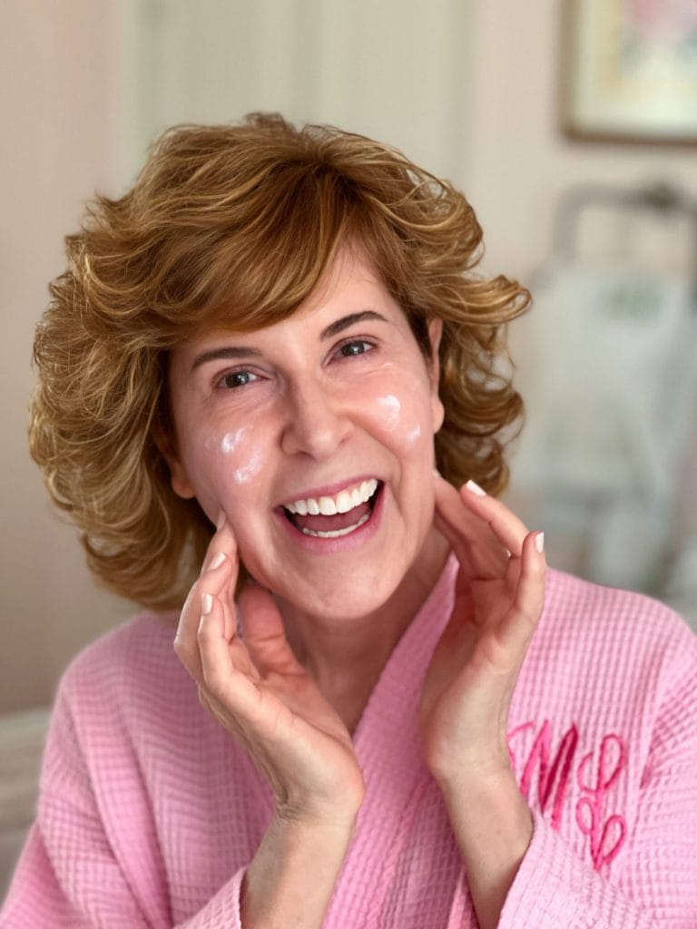 woman over 50 dressed in pink robe putting on makeup primer