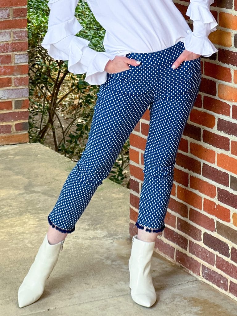 woman wearing white boots and navy polka dot ankle pants with pom pom hem