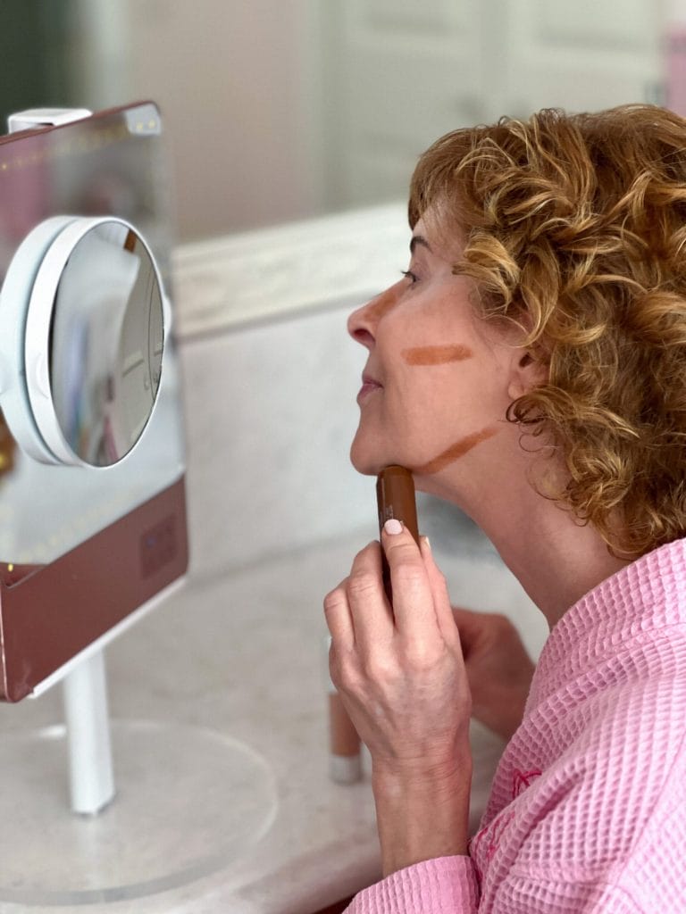woman looking into a mirror and applying contour to her face