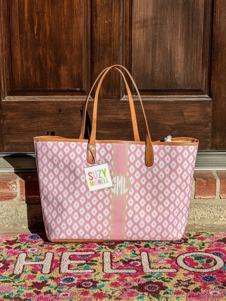 A pink monogrammed tote with a pastel bag tag sitting on a spring floral doormat