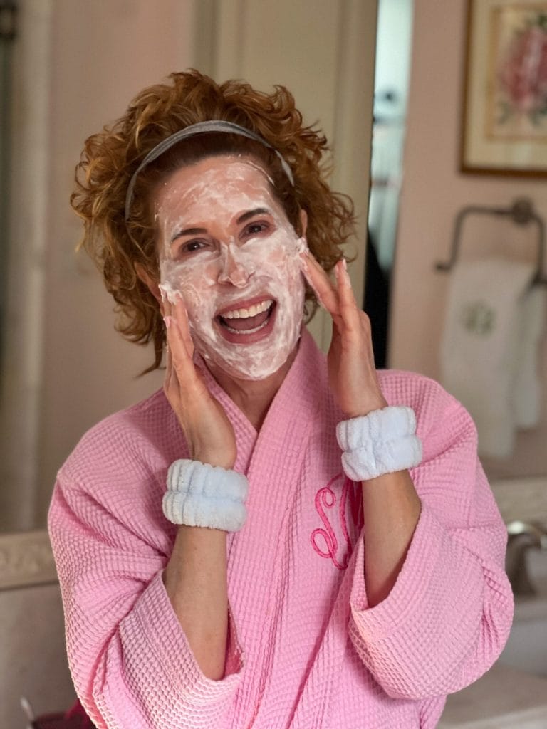 woman over 50 dressed in pink robe washing her face