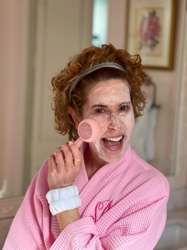 woman over 50 dressed in pink robe using Clean Smart Facial Cleansing Device - PMD
