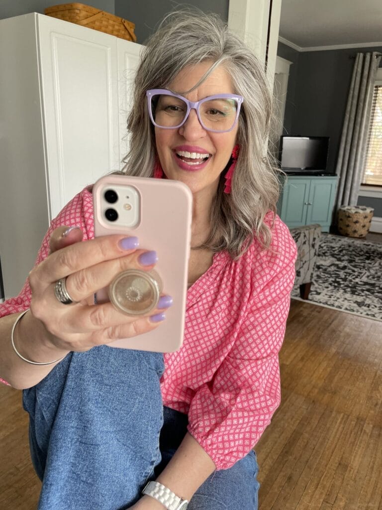 woman wearing pink top and big glasses looking at her cell phone