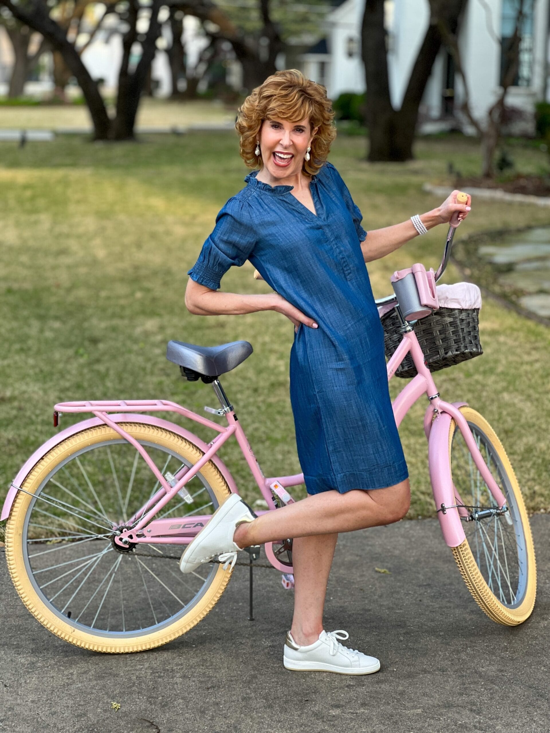 woman wearing denim shift dress standing next to a pink bike