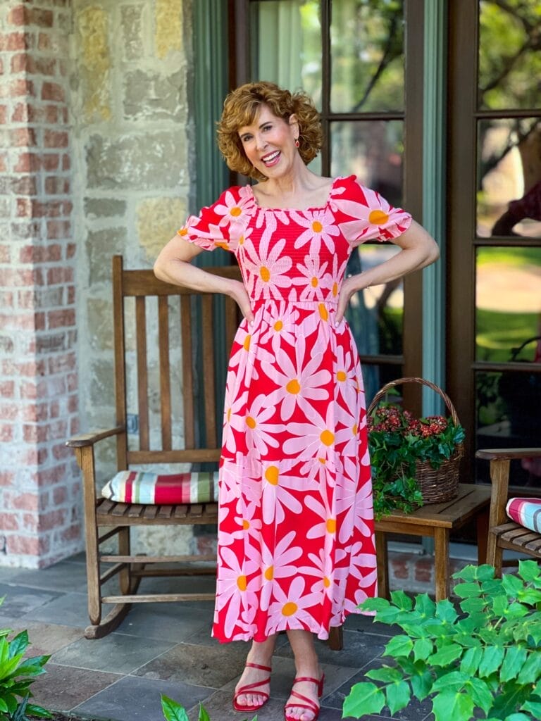 woman over 50 wearing a red amazon dress with daisies on it standing with her hands on her hips on front porch