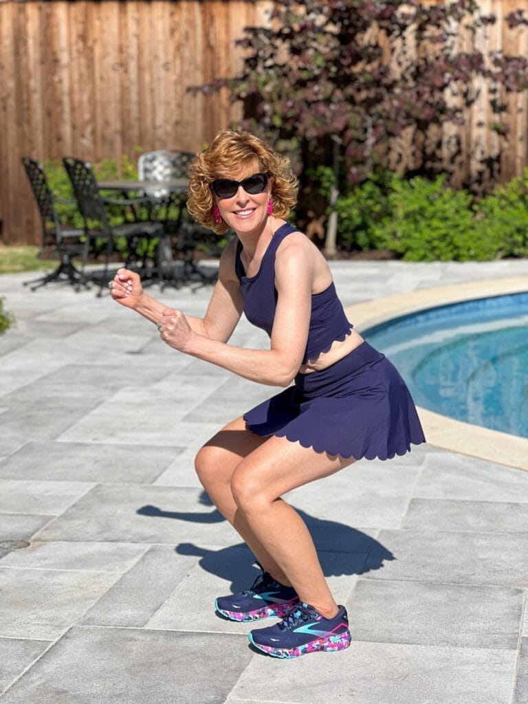 woman over 50 wearing navy blue scalloped workout set standing by a pool demonstrating a squat