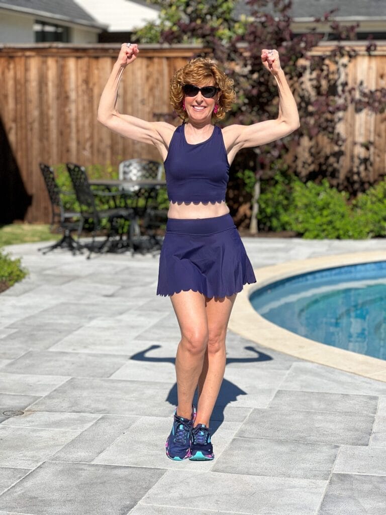 woman over 50 wearing navy blue scalloped workout set standing by a pool showing her muscles