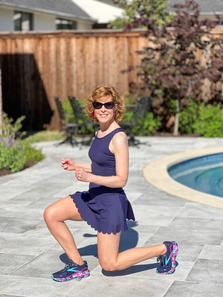 woman over 50 wearing navy blue scalloped workout set standing by a pool demonstrating a lunge