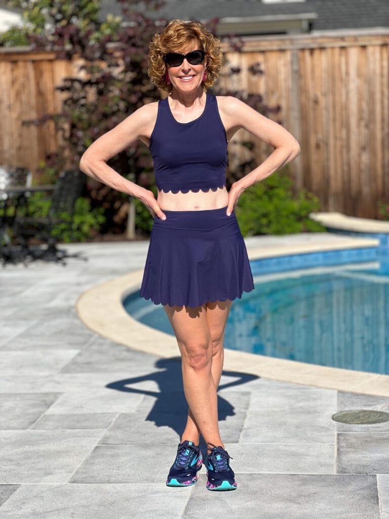 woman over 50 wearing navy blue scalloped workout set standing by a pool wearing naby blue workout set