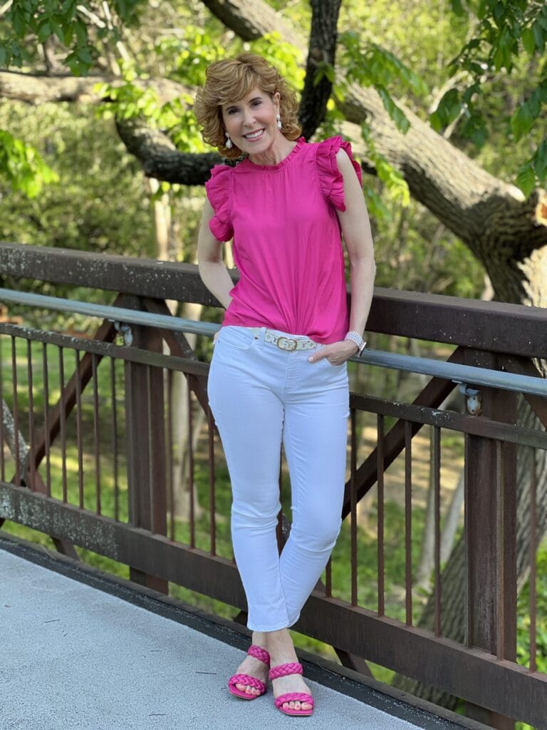 woman wearing pink ruffle sleeve top and white jeans standing on a bridge