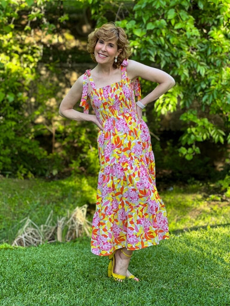 woman wearing yellow, pink, and orange smocked top dress from Avara standing with her hands on hips in the outdoors