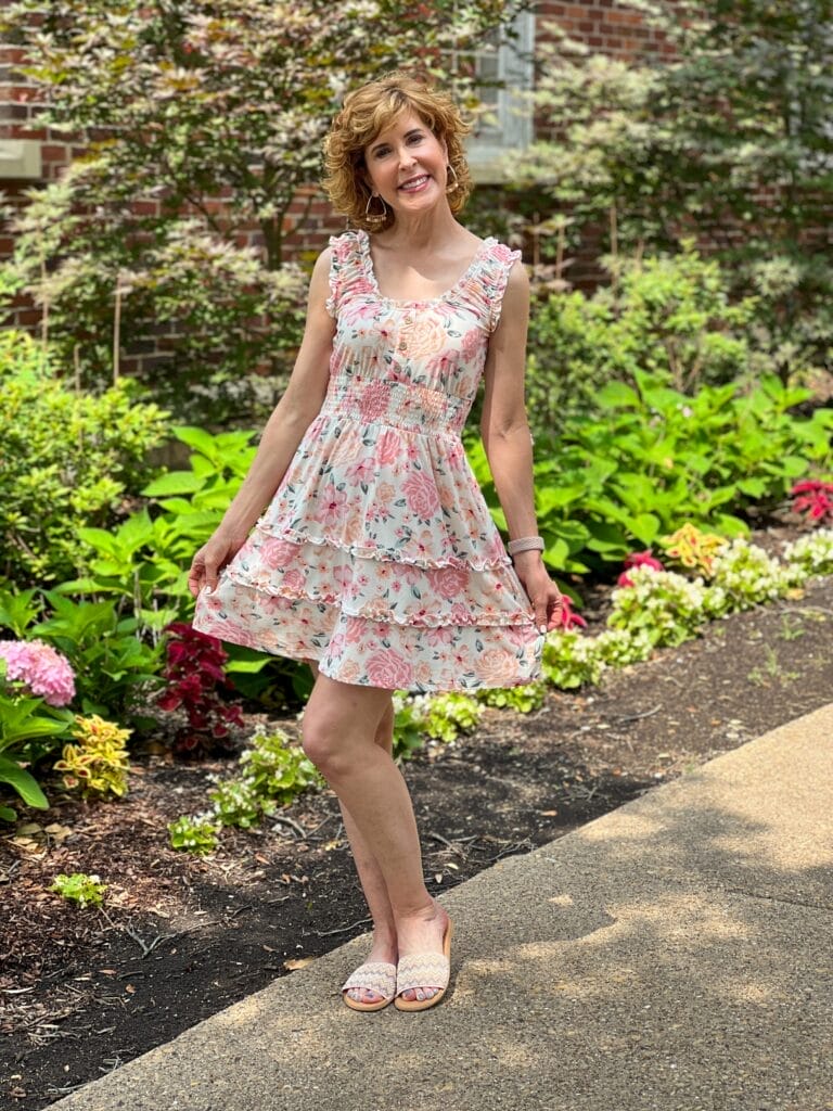 woman standing in a garden holding out the skirt of her No Boundaries Juniors Sleeveless Ruffle Dress
