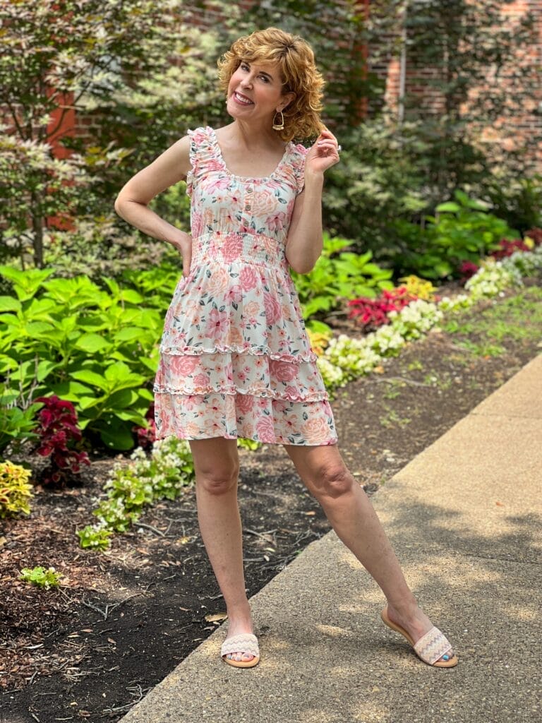 Woman standing in a garden with hand on hip and leg outstretched wearing No Boundaries Juniors Sleeveless Ruffle Dress
