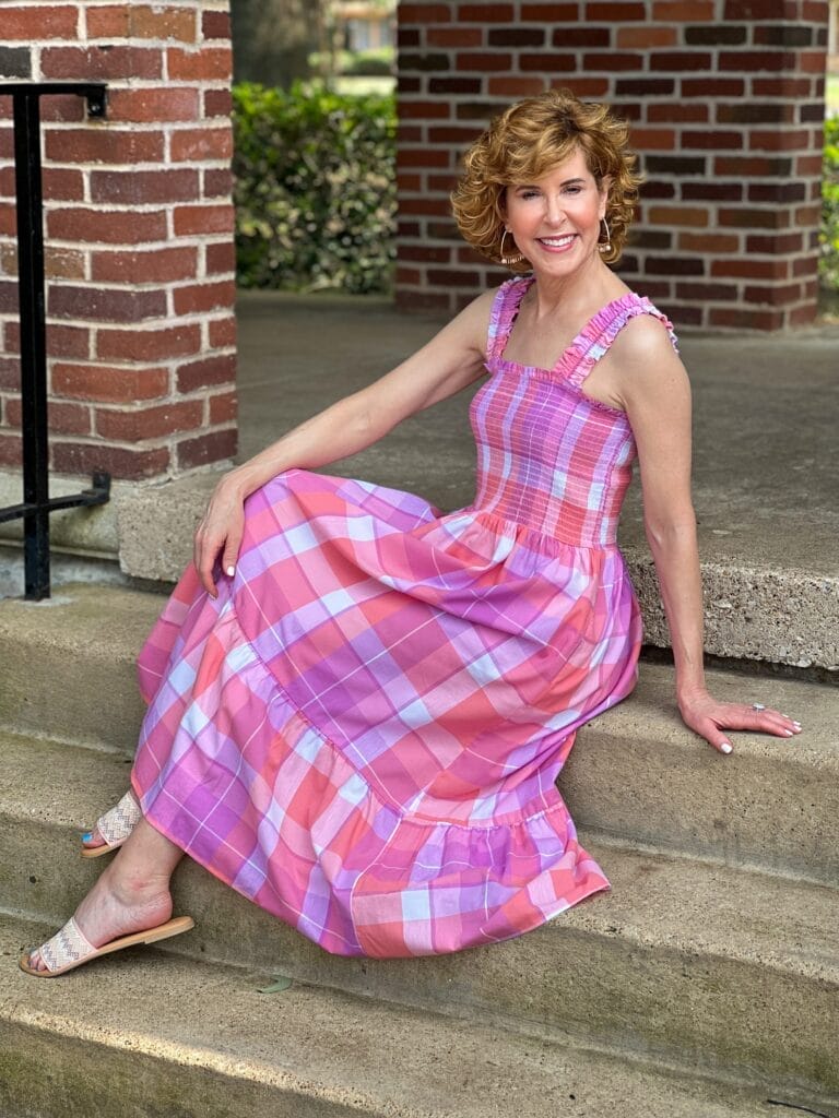 woman sitting on stairs outdoors wearing Time and Tru Women's Smocked Midi Dress with Ruffle Straps from Walmart in pink madras plaid
