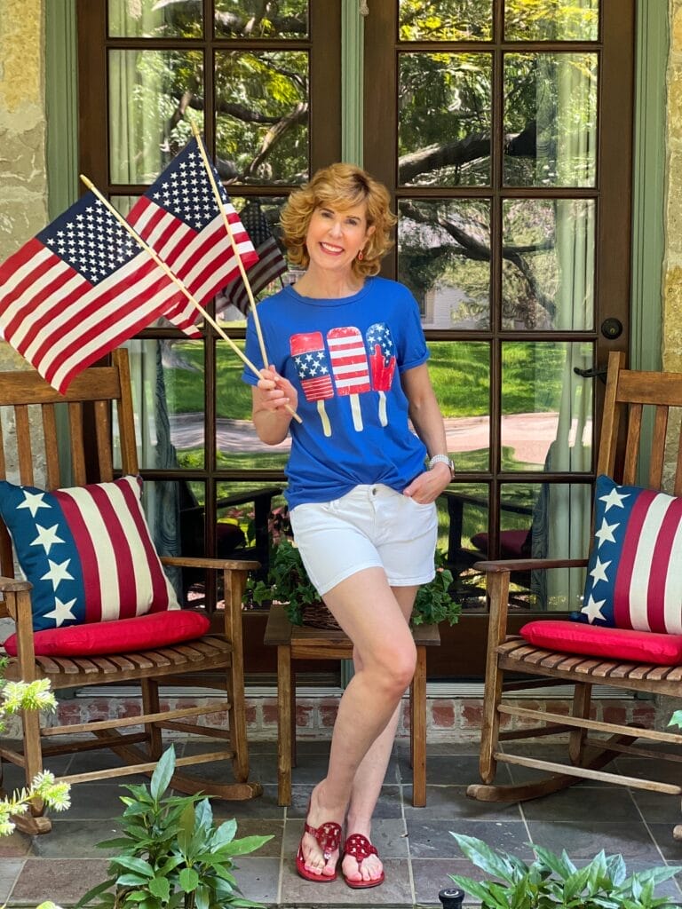 woman on front porch in patriotic attire holding american flags