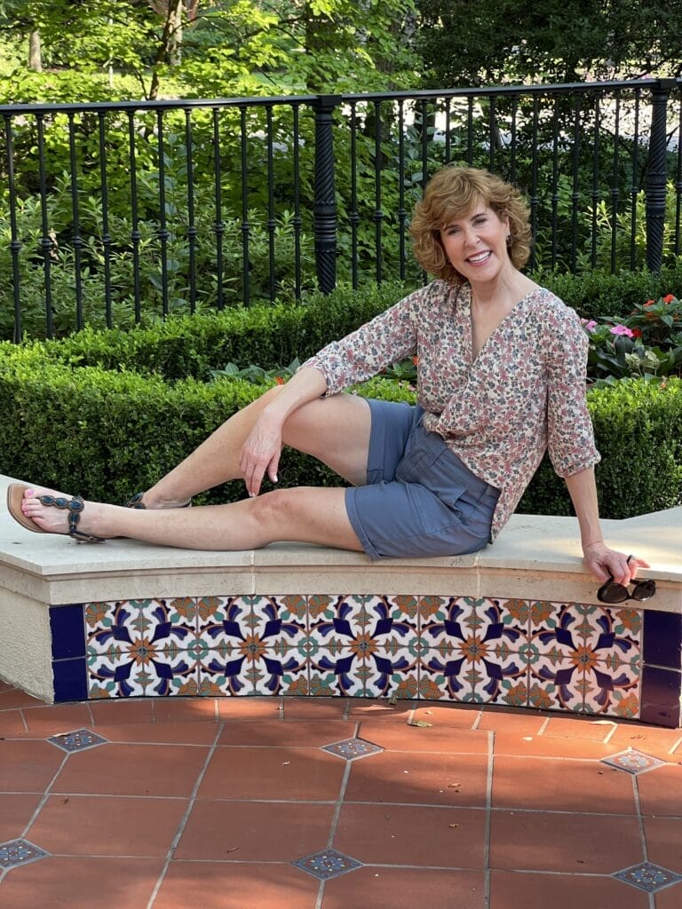 woman sitting on a ledge wearing blue cargo shorts and a pintuck blouse from nydj