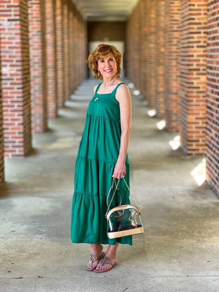 woman standing in green sleeveless dress holding clear stadium purse